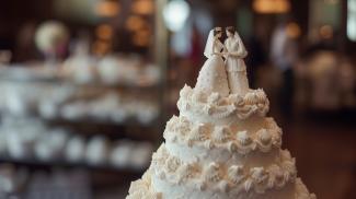 Two women wedding cake toppers in bridal dresses on the top of a white wedding cake