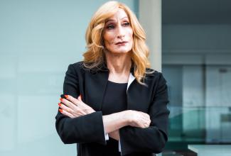 Transgender businesswoman with blond hair, a black suit, and a serious, pensive look on her face