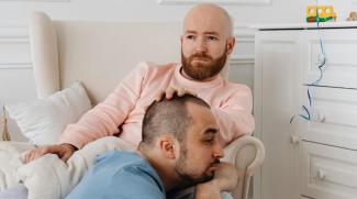 A gay male couple with sad facial expressions sitting in their child’s bedroom.